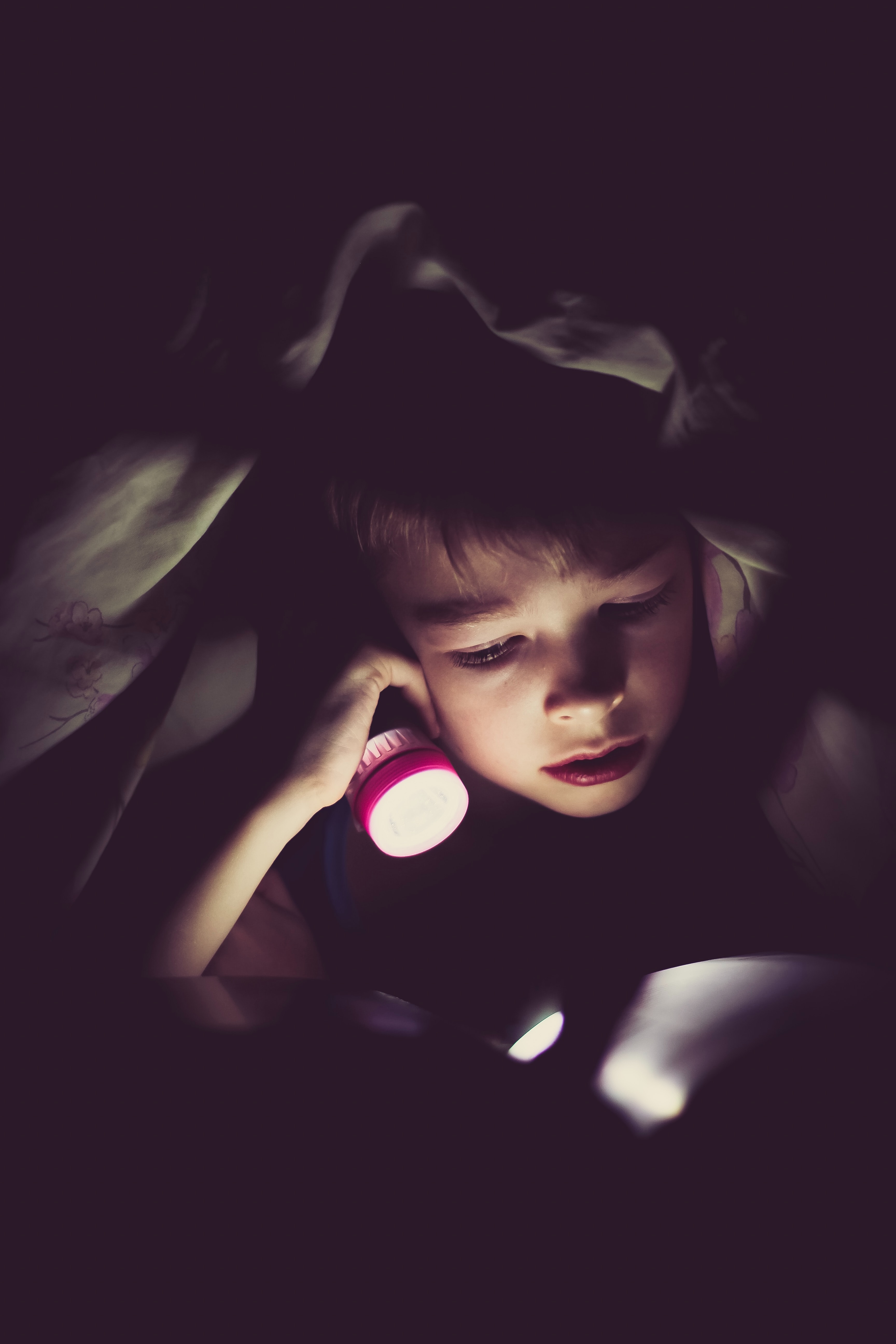 child reading by flashlight in bed by Klim Sergeev